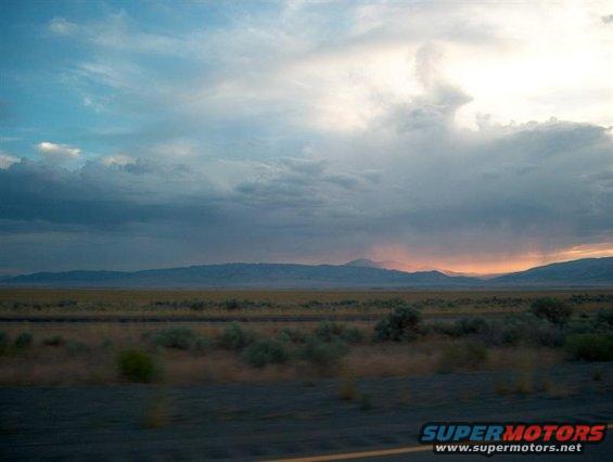 Desert landscape with mountains under a dramatic cloudy sky at sunset