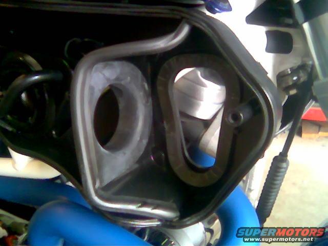 Motorcycle air intake housing with a curved filter element inside. Blue pipes are visible below