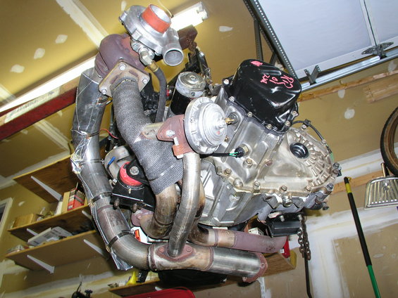 Engine assembly with turbocharger and exhaust manifold, suspended in a garage