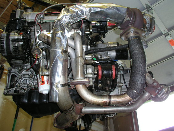 Turbocharged engine with silver heat wrap on exhaust manifold and black exhaust wrap on downpipe