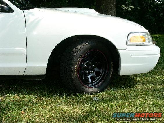 White 2001 Ford Crown Victoria front fender and black wheel with red trim, parked on grass