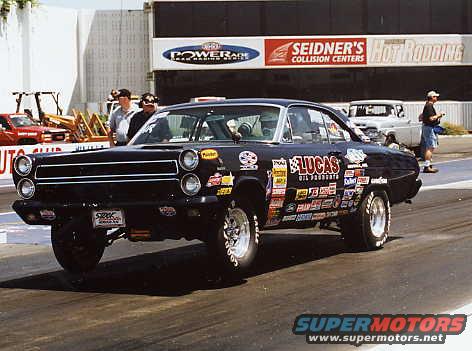 Black 1966 Ford Fairlane drag car, front 3/4 view, covered in decals, on a race track