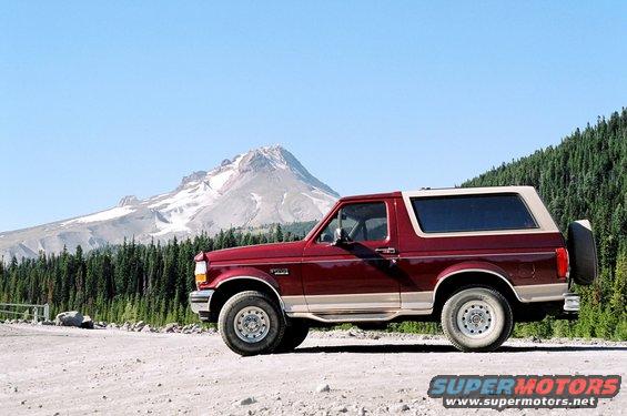 Red Ford Bronco parked on a dirt road with a mountain and forest in the background