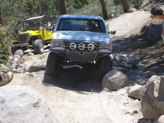 Silver off-road truck with custom bumper and lights, driving on a rocky trail