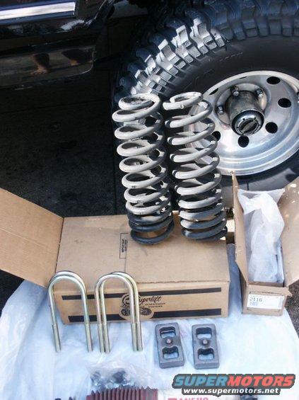 Suspension lift kit parts including coil springs, U-bolts, and blocks next to a vehicle tire
