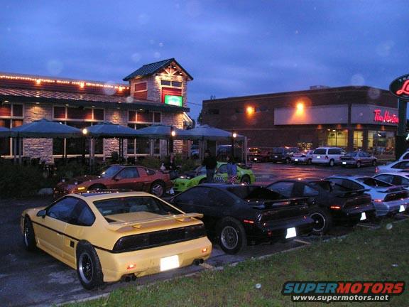 Yellow 1984 Pontiac Fiero rear view parked in a lot with other Fieros