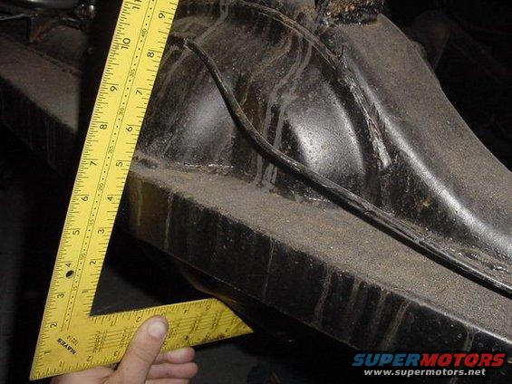 Yellow speed square measuring a black metal vehicle suspension part