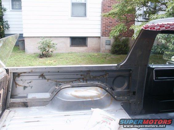 Interior of a truck bed, showing the wheel well and side panel. Some rust and dirt are visible