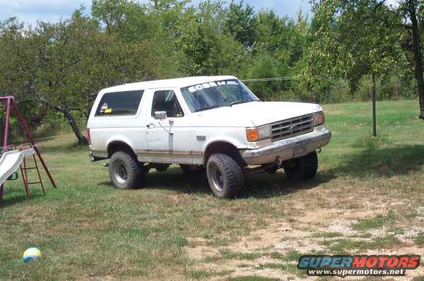 White 1988 Ford Bronco with a banner on the windshield parked on grass