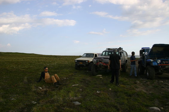 Three modified off-road Jeeps parked on a grassy hill under a cloudy sky