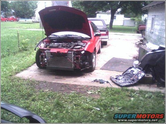 Red car with hood open, front bumper removed, parked outside