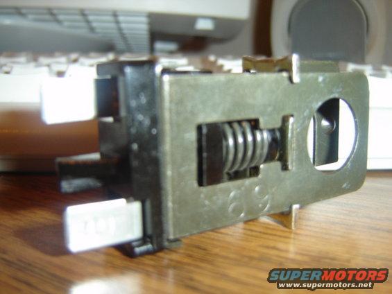 Metal switch with visible spring and two white plastic connectors, one with faint text