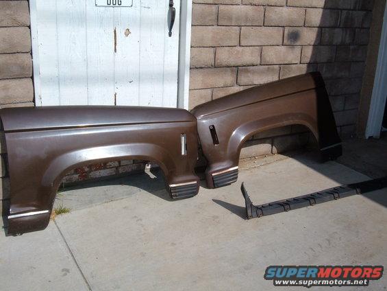 Two brown fender flares and a running board are on the ground in front of a brick wall and a white door