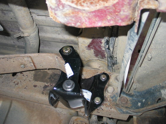 Aftermarket suspension brackets bolted to rusty vehicle frame with visible wiring and exhaust pipe