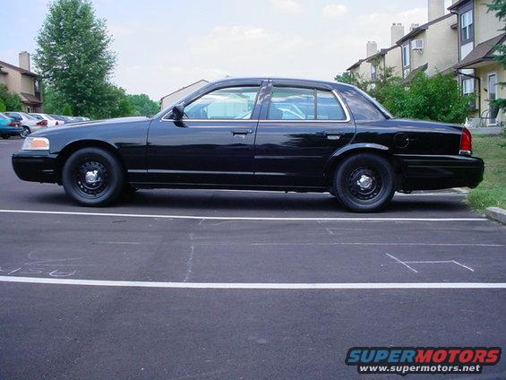 Black sedan parked in a lot. Looks like a Crown Victoria, maybe a 2000 model