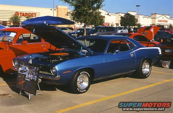 Blue 1970 Plymouth Barracuda with hood open, parked next to a red car. Sign says 440-6 CUDA