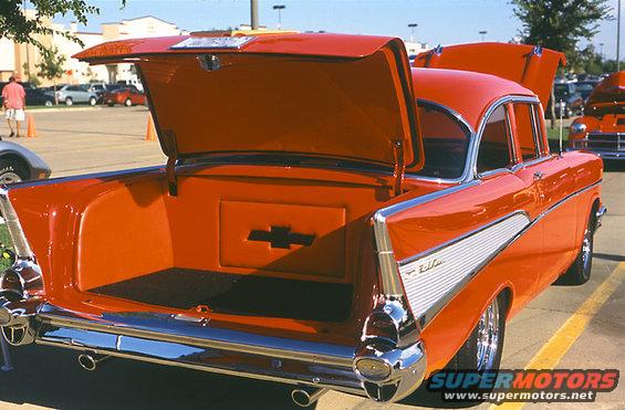 Orange 1957 Chevrolet Bel Air with open trunk and hood. Chrome trim and Chevrolet logo visible