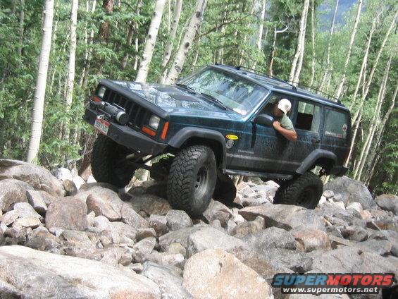 Dark green 1997 Jeep Cherokee off-roading over rocks, front 3/4 view
