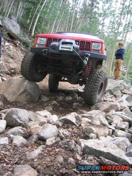 Red 1997 Jeep Cherokee climbing over rocks on a trail