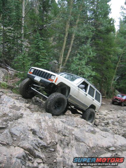 White 1997 Jeep Cherokee climbing a steep, rocky off-road trail with a red Jeep in the background