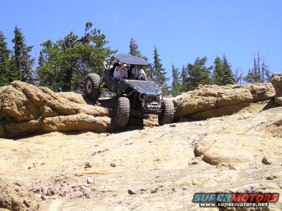 Off-road buggy with a roll cage climbing over large rocks on a sunny day