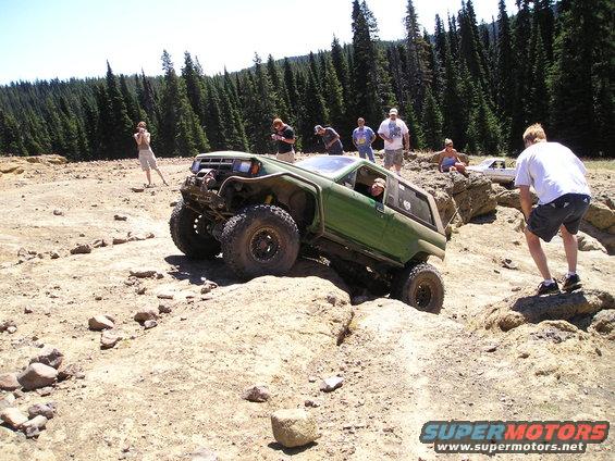 Green 1989 Ford Bronco off-roading on a rocky trail with people watching