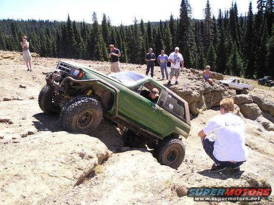 Green 1989 Ford Bronco climbing rocky terrain, 3/4 front view
