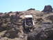 1989 Ford Bronco - A white SUV navigates a challenging rocky incline, with a person observing the ascent.