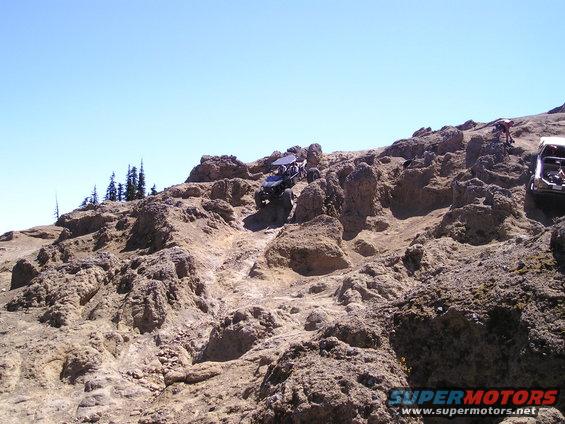 Off-road vehicles navigating a steep, rocky terrain under a clear blue sky