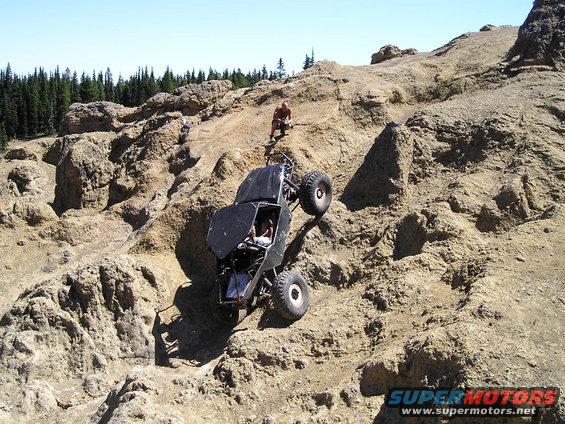Off-road buggy crawling up a steep, rocky hill with a person watching from above