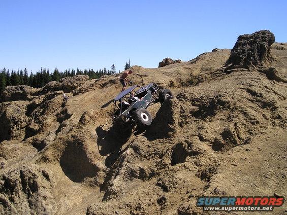Off-road buggy with roll cage climbing a steep, rocky incline under a clear blue sky