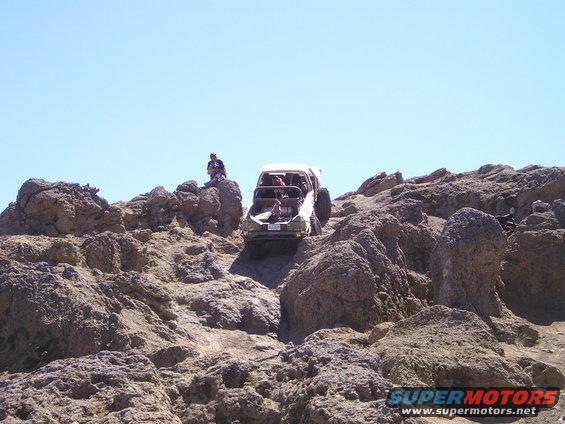 1989 Ford Bronco navigating a steep, rocky trail with people watching