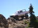 1989 Ford Bronco - A modified pickup truck navigates a challenging rocky terrain under a clear blue sky.