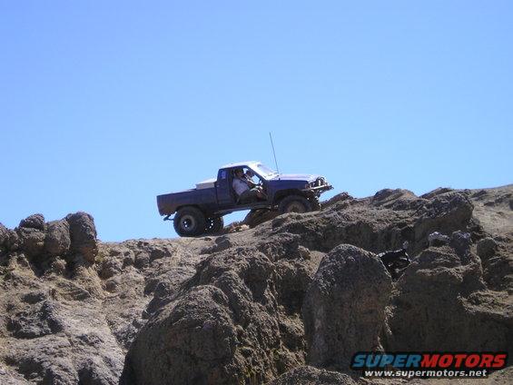 Blue pickup truck with a white toolbox in the bed driving over rocks