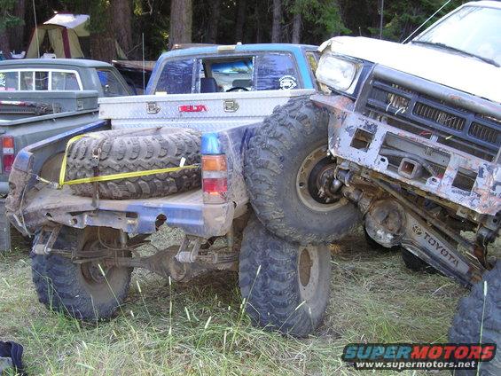 Two off-road trucks are stuck together, one with a spare tire in the bed