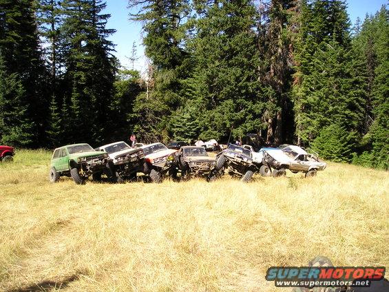 Group of off-road vehicles parked in a dry grassy field with trees in the background