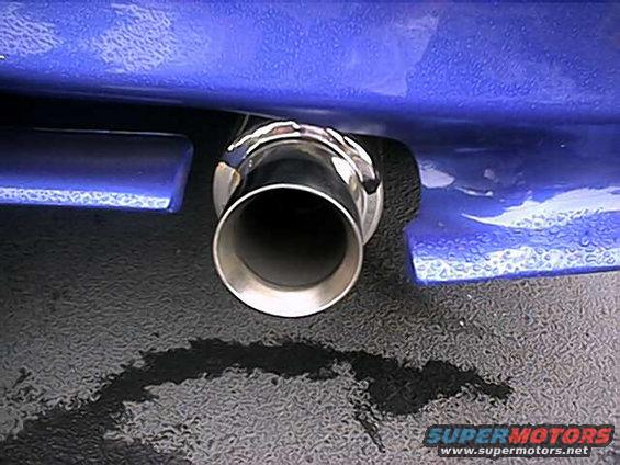 Close-up of a chrome exhaust tip on a blue car bumper, with black fluid spilled on the ground