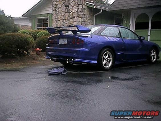 Blue 1993 Ford Probe with a large rear spoiler and aftermarket exhaust tips parked on a wet driveway