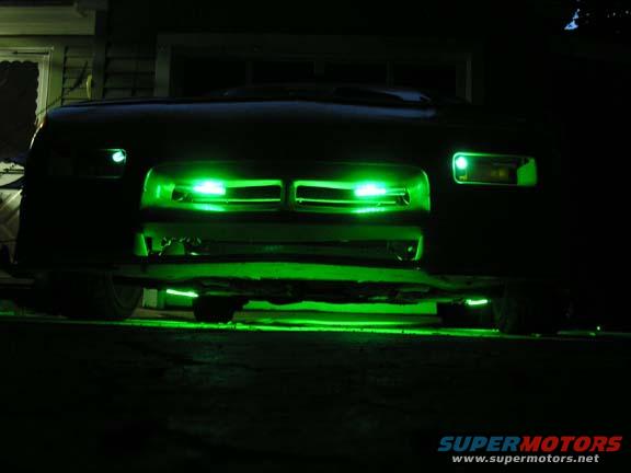 Front of a dark-colored car with green underglow lighting and green lights in the grille