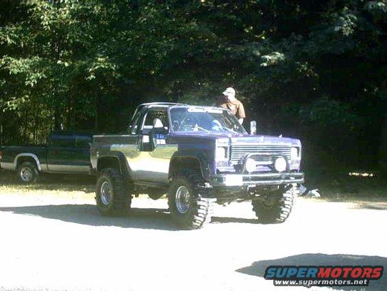 Lifted pickup truck with chrome trim and off-road tires parked next to a dark green pickup truck