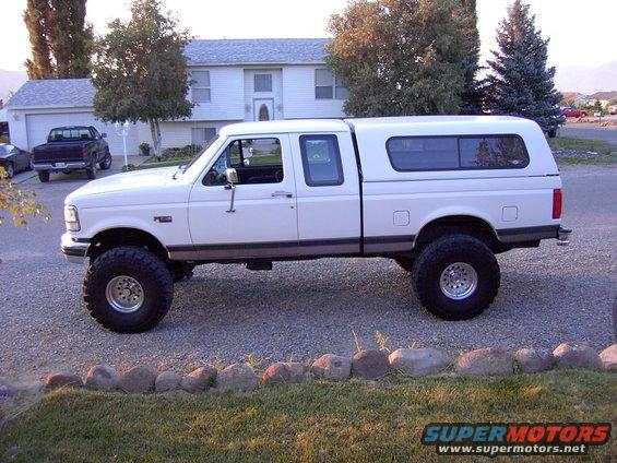 1992 Ford F-150 crew cab pickup truck, lifted with large tires and a white camper shell, parked in a driveway