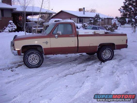 Two-tone pickup truck parked in snow, with another car visible in the background