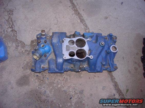 Blue intake manifold with a silver gasket and various ports, resting on a concrete surface
