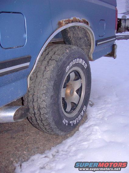 Blue pickup truck rear wheel well with rust, showing a Courser Radial LT tire and a chrome exhaust pipe