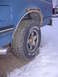 1992 Ford F-150 - A blue pickup truck's rear wheel well shows significant rust and a Courser Radial LT tire, with a chrome exhaust pipe visible.