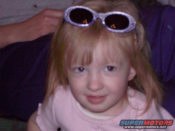 Young girl with blonde hair and blue eyes wearing a pink shirt, with sparkly sunglasses on her head