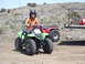 1992 Ford F-150 - A child wearing a helmet rides a green ATV in a dusty, outdoor setting, with another ATV visible behind.