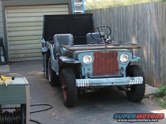 Jeep CJ-3B with open hood, parked outside near a fence and garage