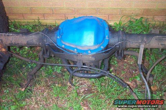 Ford rear axle assembly with blue differential cover, brake lines, and part of a tire visible