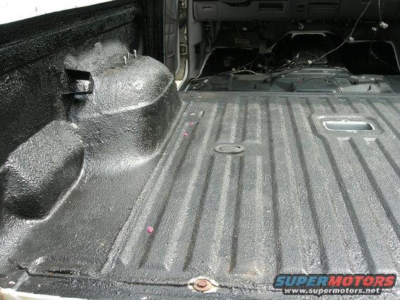 Truck bed interior with black spray-on liner, showing wheel well and interior cabin